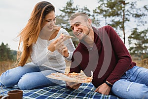 Young couple sitting on park bench and eating pizza.Fast food.Woman and man having picnic at sunset. Guys relaxing and enjoying