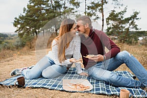 Young couple sitting on park bench and eating pizza.Fast food.Woman and man having picnic at sunset. Guys relaxing and enjoying