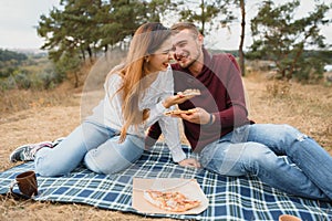 Young couple sitting on park bench and eating pizza.Fast food.Woman and man having picnic at sunset. Guys relaxing and enjoying