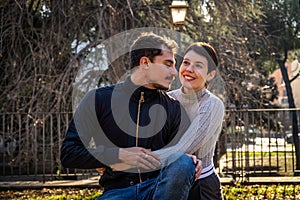 The young couple is sitting on a park bench in Rome.