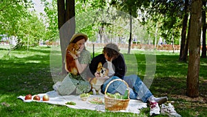 A young couple is sitting in the park on a picnic and stroking their pet dogs on the head. Picnic in nature