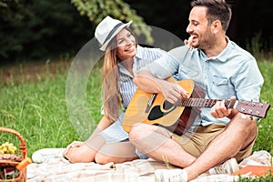 Young couple sitting on a picnic blanket, playing guitar and singing