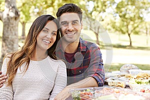 Young couple sitting at picnic table smiling to camera