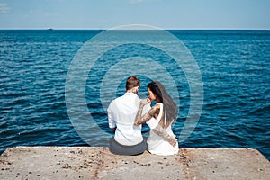 Young couple are sitting on the pier by the sea