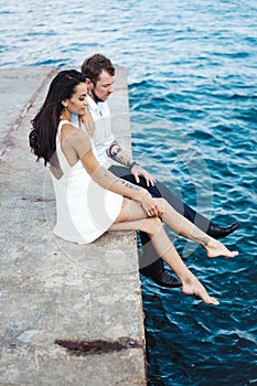 Young couple are sitting on the pier by the sea