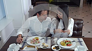 Young couple sitting in the restaurant and taking pictures of the food with mobile phone