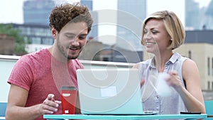 Young Couple Sitting On Roof Terrace Using Laptop