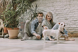 Young couple sitting at rustic living room floor and playing with dog