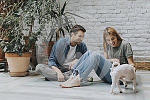 Young couple sitting at rustic living room floor and playing with dog