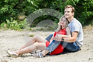 Young couple sitting on the sand smiling and hugging