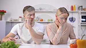 Young couple sitting silently in kitchen after argument, crisis in relationship