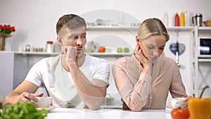 Young couple sitting silently in kitchen after argument, crisis in relationship