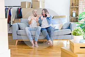 Young couple sitting on the sofa arround cardboard boxes moving to a new house afraid and terrified with fear expression stop