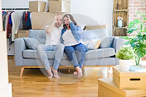 Young couple sitting on the sofa arround cardboard boxes moving to a new house doing ok gesture shocked with surprised face, eye