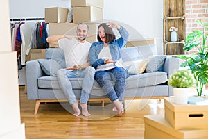 Young couple sitting on the sofa arround cardboard boxes moving to a new house gesturing with hands showing big and large size