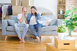 Young couple sitting on the sofa arround cardboard boxes moving to a new house with hand on head for pain in head because stress