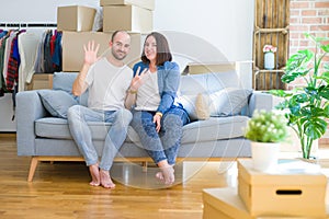 Young couple sitting on the sofa arround cardboard boxes moving to a new house showing and pointing up with fingers number nine