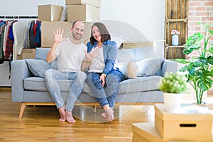 Young couple sitting on the sofa arround cardboard boxes moving to a new house showing and pointing up with fingers number ten