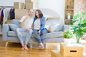 Young couple sitting on the sofa arround cardboard boxes moving to a new house showing and pointing up with fingers number two