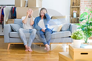 Young couple sitting on the sofa arround cardboard boxes moving to a new house suffering from headache desperate and stressed