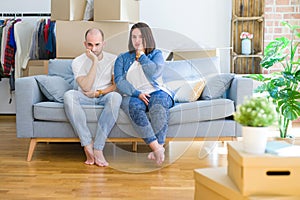 Young couple sitting on the sofa arround cardboard boxes moving to a new house thinking looking tired and bored with depression