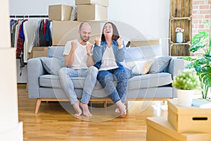 Young couple sitting on the sofa arround cardboard boxes moving to a new house very happy and excited doing winner gesture with