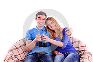 Young couple sitting on a sofa and drinking Coca Cola isolated