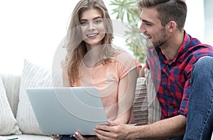 Young couple sitting on sofa and looking at pictures on the laptop.