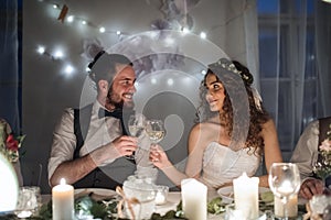 A young couple sitting at a table on a wedding, clinking glasses.