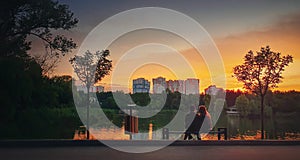 Young couple sitting together on the bench in the park near the lake against bright sunset. Romantic lifestyle background,