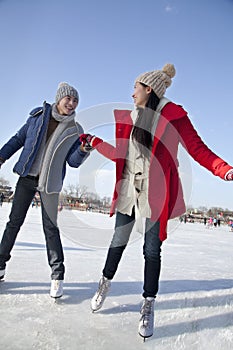 Young couple skating at ice rink, holding hands