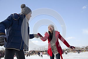 Young couple skating at ice rink, holding hands