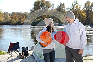 Young couple with sleeping bags near camping tent outdoors.