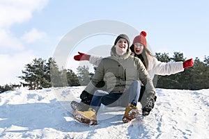 Young couple slide down the snow slide. Winter sunny day. Man and womana gainst the background of the forest and the blue sky photo