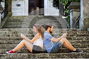 Young couple with smartphones sitting on stairs in town.