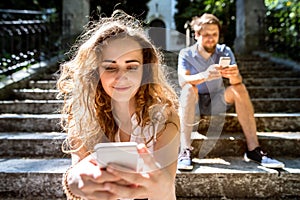 Young couple with smartphones sitting on stairs in town.