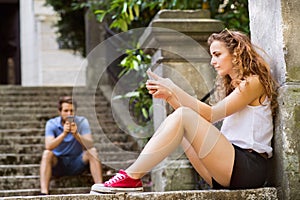Young couple with smartphones sitting on stairs in town.