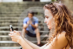 Young couple with smartphones sitting on stairs in town.