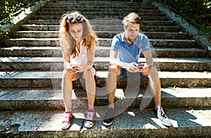 Young couple with smartphones sitting on stairs in town.