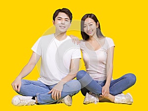 Young couple smiling at camera while woman putting her hand on male shoulder.Isolated on yellow background