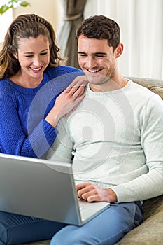 Young couple smiling face to face on sofa and using laptop