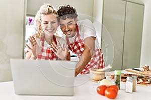Young couple smiling happy having video call using laptop at kitchen
