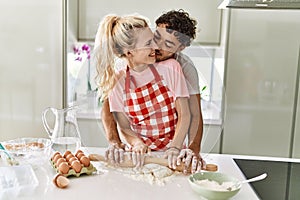 Young couple smiling happy kneading dough with hands at kitchen