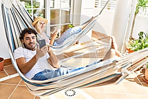 Young couple smiling happy relaxed using smartphone and reading book