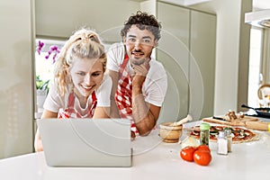 Young couple smiling happy using laptop at kitchen