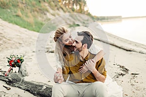 A young couple is smiling and hugging on the beach. Rustic wedding ceremony outdoors. Bride and groom look at each other