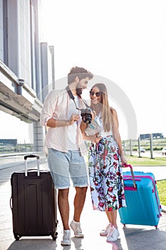 Young couple smiling and looking at photos on camera in front of an airport terminal