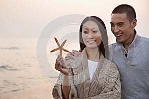 Young Couple Smiling and Looking At a Seashell