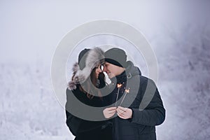 Young couple with sparklers in winter forest. Smiling family with bengal lights.