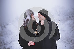 Young couple with sparklers in winter forest. Smiling family with bengal lights.